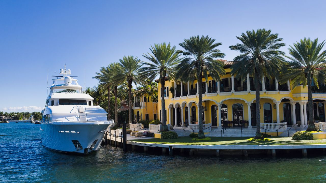 about-01 A stunning view of a luxury yacht docked beside a grand mansion in Fort Lauderdale, Florida.